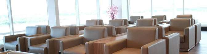 The seating area in Concordia Lounge at Achmad Yani International Airport features comfortable armchairs with individual tables and large windows.
