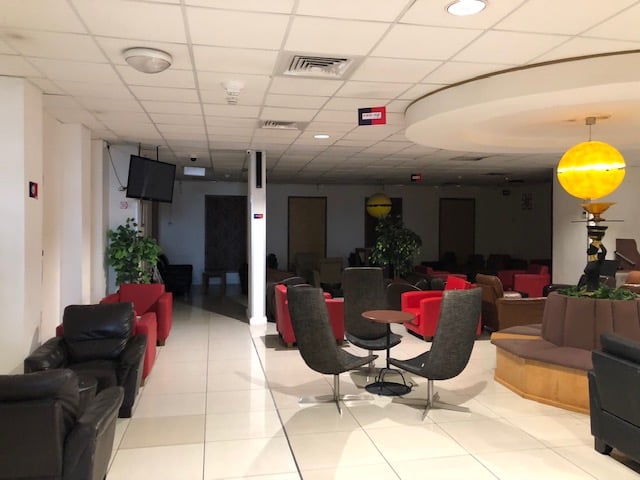 Seating area in Adinkra Lounge at Kotoka International Airport features various chairs and tables, with a television and plants for ambiance.