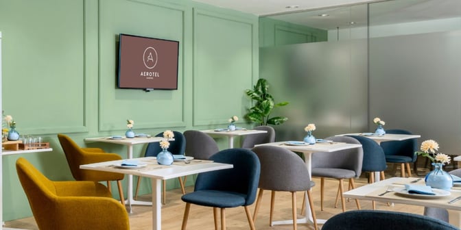 The dining area at The Hub in Madrid Barajas Airport features table seating with place settings and decorative plants.