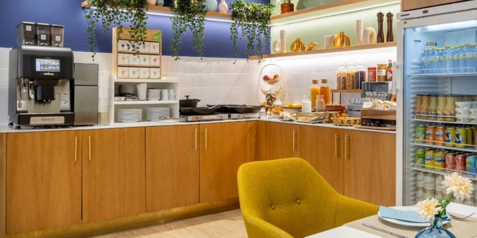 The self-serve area at The Hub in Madrid Barajas Airport offers a variety of beverages and snacks, including a coffee machine and refrigerated drinks.