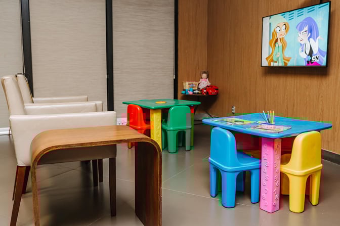 The children's play area in the Aeroportos VIP Club features colorful tables, chairs, toys, and a TV showing cartoons.