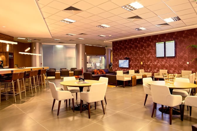 The Aeroportos VIP Club lounge at Brasilia International Airport features a bar with high seating and a seating area with tables and chairs.