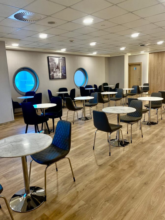 Seating area in Ahlein Premium Lounge at Cairo International Airport features round tables and chairs, providing a space for relaxation and dining.