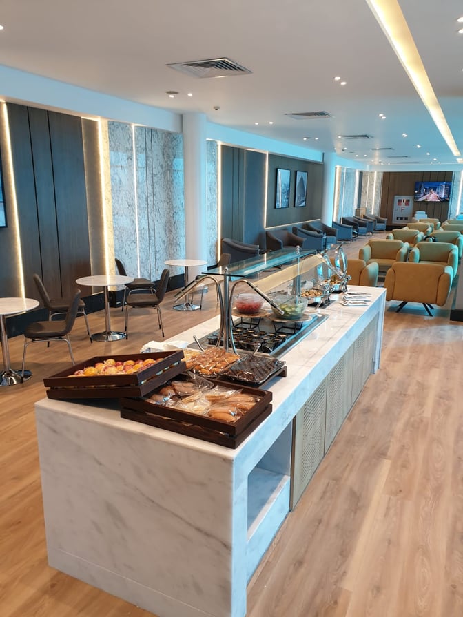 The Ahlein Premium Lounge at Cairo International Airport features a self-serve food station with pastries and seating areas for travelers.