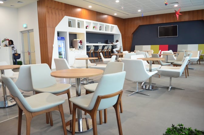 The Akwaaba Lounge at Kotoka International Airport features a seating area with tables and chairs, a beverage station, and a reception desk.