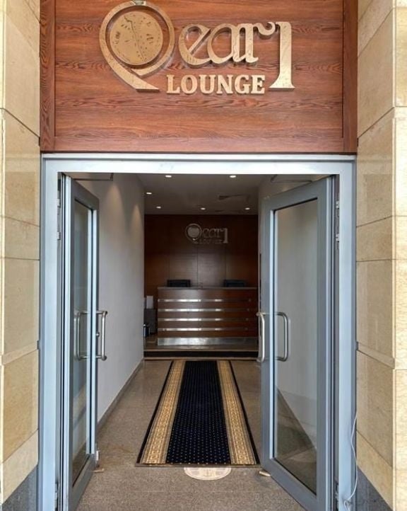 The entrance to the Pearl Lounge at Alexandria International Airport features double glass doors leading to a reception desk.