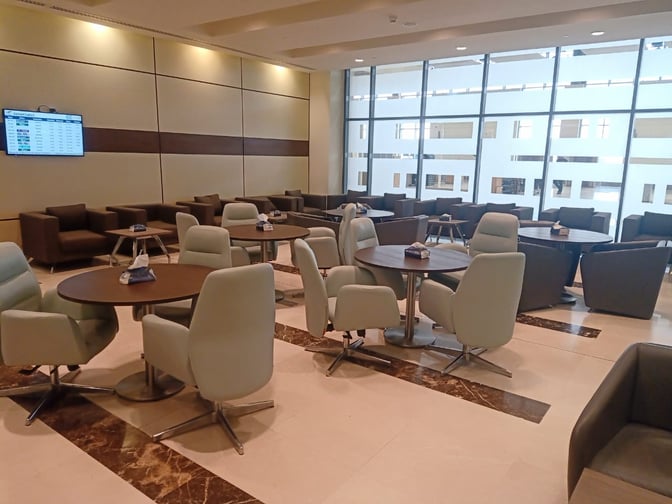 The seating area in the Pearl Lounge at Alexandria Airport features round tables with chairs and sofas, offering a view of the terminal.