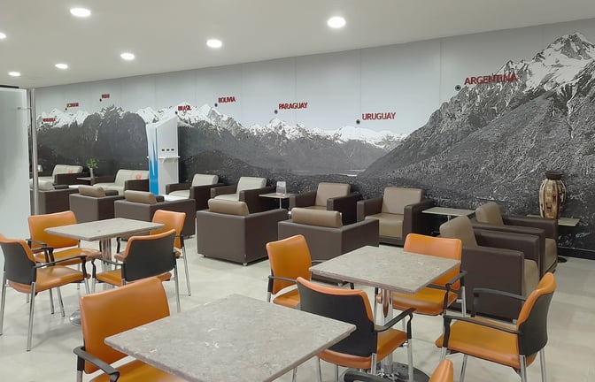 The Avianca Lounge in Cali features a seating area with tables and chairs, set against a wall mural of mountains.