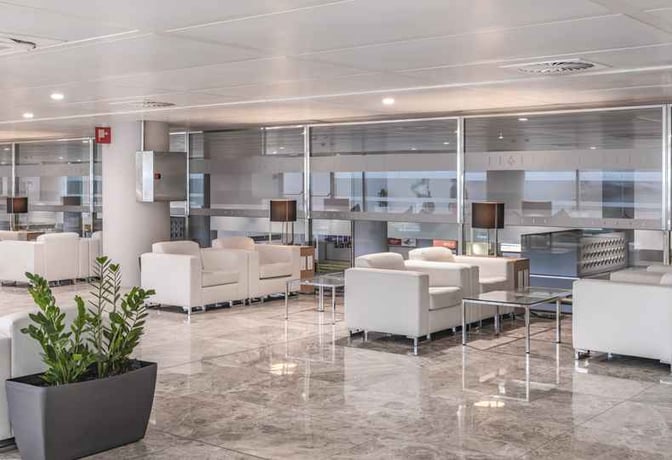 The seating area in Sala VIP Costa Blanca at Alicante-Elche Airport features comfortable armchairs and tables with views of the terminal.