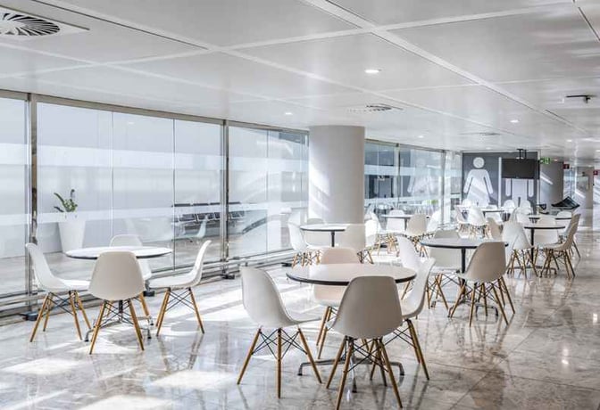 The seating area in the Sala VIP Costa Blanca at Alicante-Elche Airport features round tables and chairs near large windows.