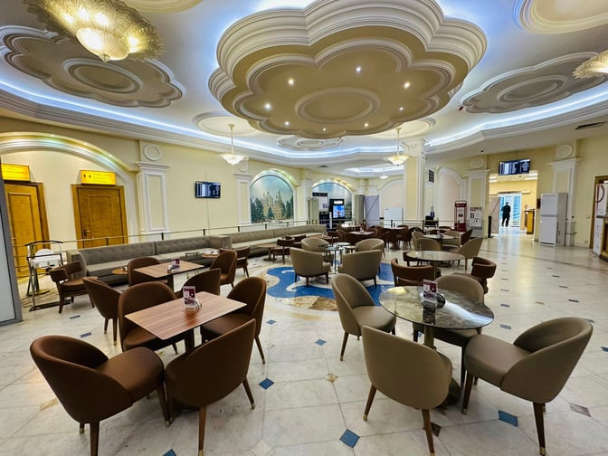 The Primeclass Lounge at Almaty International Airport features a seating area with tables and chairs, providing a comfortable waiting space.