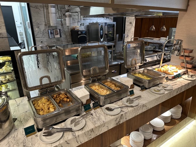 The Extime Business Lounge at Almaty International Airport features a self-serve buffet with hot food options and ample dishware.