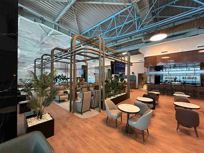 The Extime Business Lounge at Almaty International Airport features a seating area with tables and a bar offering various beverages.