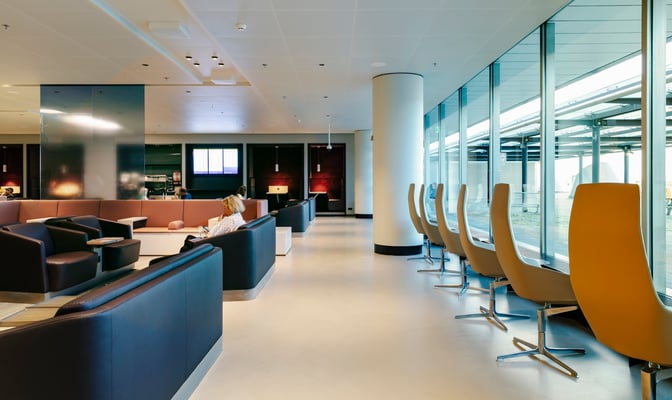 The Aspire Lounge at Amsterdam Schiphol Airport features comfortable seating areas and high-backed chairs overlooking the tarmac near Gate 26.