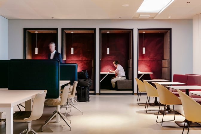 The Aspire Lounge at Amsterdam Schiphol Airport features semi-private booth seating with tables, ideal for working or relaxing near Gate 26.