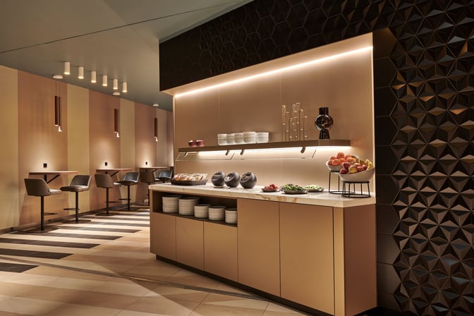 The Aspire Lounge at Amsterdam Schiphol Airport features a self-serve food station with fresh fruits and seating for dining.