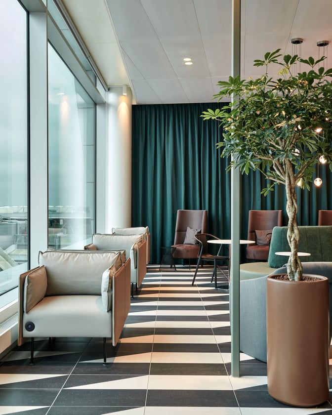 The seating area in Aspire Lounge at Amsterdam Schiphol Airport features armchairs and tables with views of the tarmac.