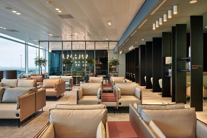 The Aspire Lounge at Amsterdam Schiphol Airport features comfortable seating with tables, offering views of the airport through large windows.