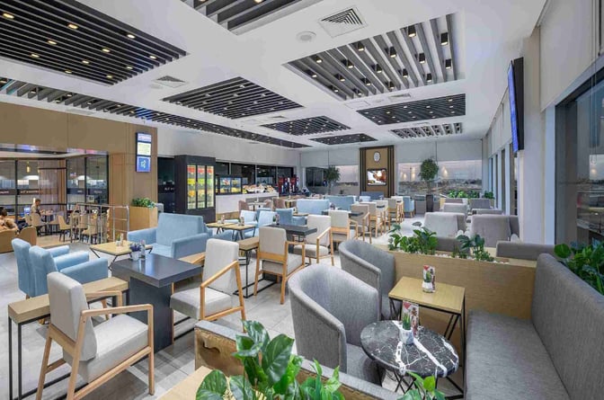 The CIP Lounge at Antalya Airport features a spacious seating area with tables, armchairs, and a self-serve beverage station.