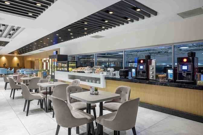 The CIP Lounge at Antalya Airport features a self-serve food and beverage area with seating, offering snacks and coffee machines.