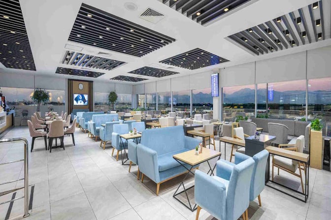 The CIP Lounge at Antalya Airport features spacious seating with tables, offering views of the runway through large windows.