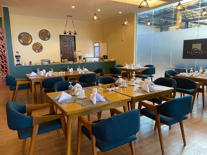 The Kilimeru Lounge at Arusha Airport features a dining area with set tables and a self-serve beverage station.