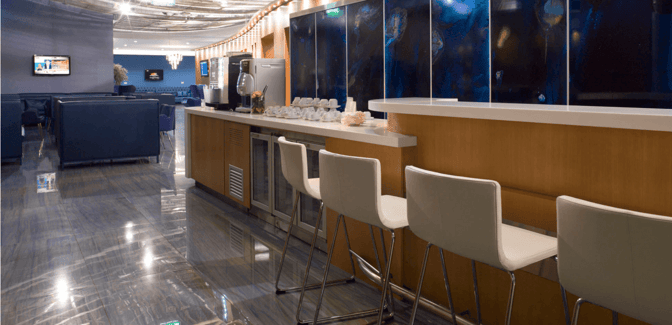 The Skyserv Aristotle Onassis Lounge features a self-serve beverage station with counter seating and a seating area with televisions.