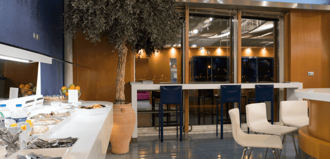The Skyserv Aristotle Onassis Lounge at Athens International Airport features a self-serve food area with seating and airport views.