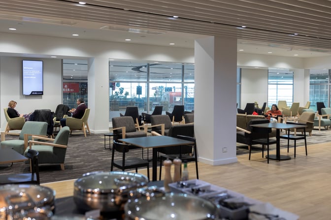 Seating area in Strata Lounge at Auckland Airport features comfortable chairs and tables with views of the terminal through large windows.