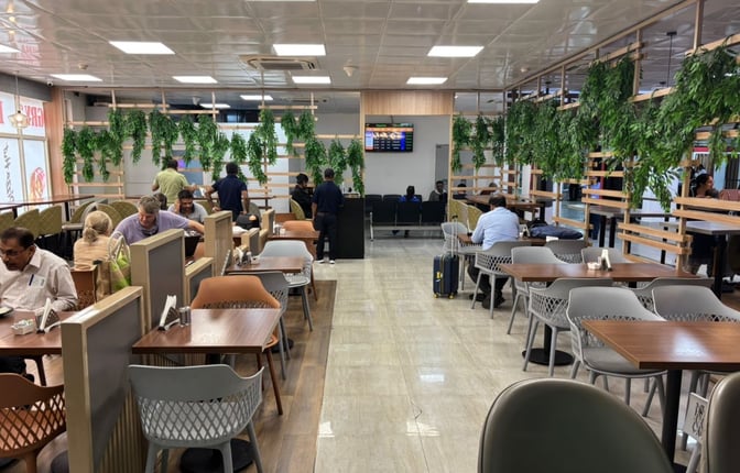 The seating area at Take Off Bar And Lounge in Bagdogra Airport features tables with chairs and semi-private partitions for dining.