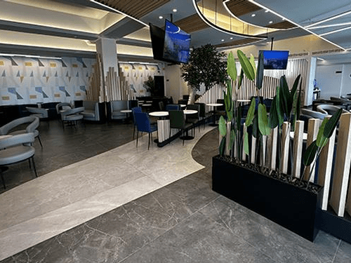 The seating area in Ahlein Premium Lounge at Baghdad International Airport features tables, chairs, and decorative plants for passenger relaxation.