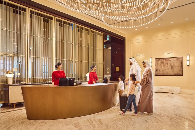 The reception area of The Pearl Lounge at Bahrain International Airport features a curved desk with staff assisting arriving guests.
