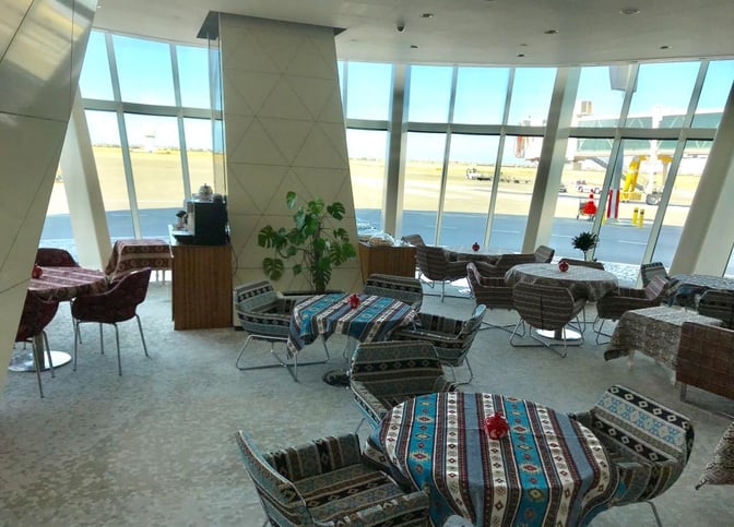 The seating area in the Premium Bank Lounge at Heydar Aliyev International Airport offers tables with runway views and patterned tablecloths.