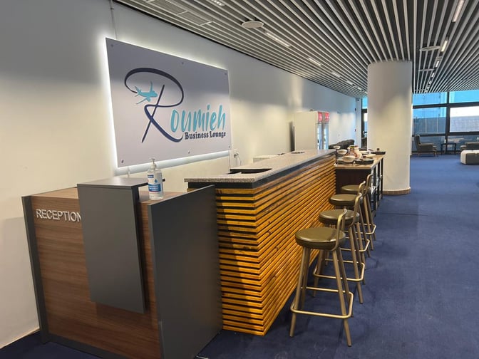 The Roumieh Business Lounge at Banjul International Airport features a reception desk and bar area with seating for guests.