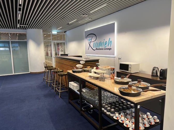 The Roumieh Business Lounge at Banjul International Airport features a self-serve food station with snacks, beverages, and seating.