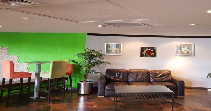 Seating area in the Airlines Executive Lounge at Grantley Adams International Airport features a sofa, high chairs, and a flight information screen.