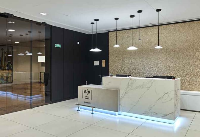 The entrance to Sala VIP Canudas at Barcelona Airport features a reception desk with overhead lighting and glass doors.