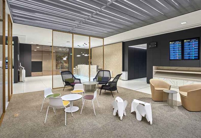 The seating area in Sala VIP Canudas at Barcelona Airport features various chairs and tables with a flight information display nearby.