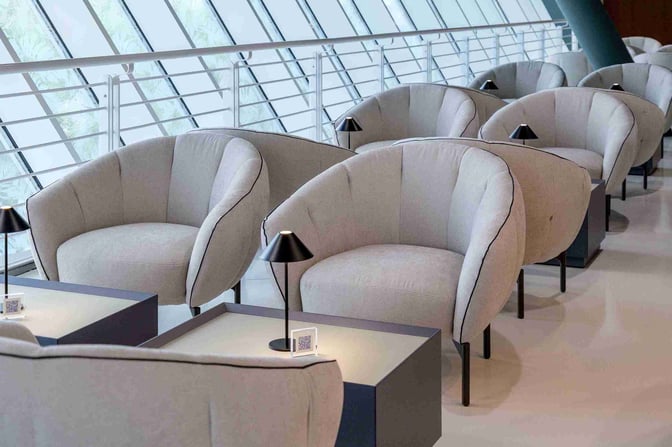 The seating area at Bari Karol Wojtyła Airport's work lounge features comfortable chairs and tables with individual lamps for personal use.