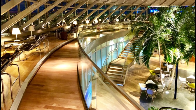 The EuroAirport Skyview Lounge features a spacious seating area with lounge chairs, tables, and a staircase leading to a lower level.