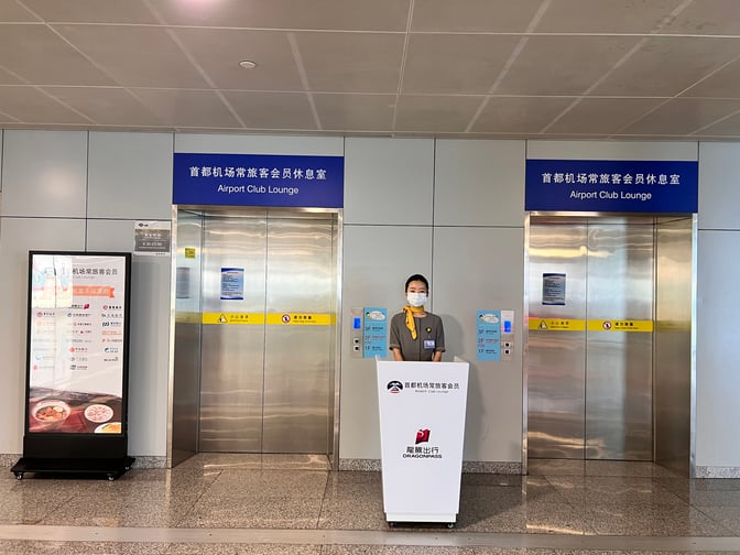 The entrance to the Airport Club Lounge at Beijing Capital International Airport features elevators and a staffed reception desk.