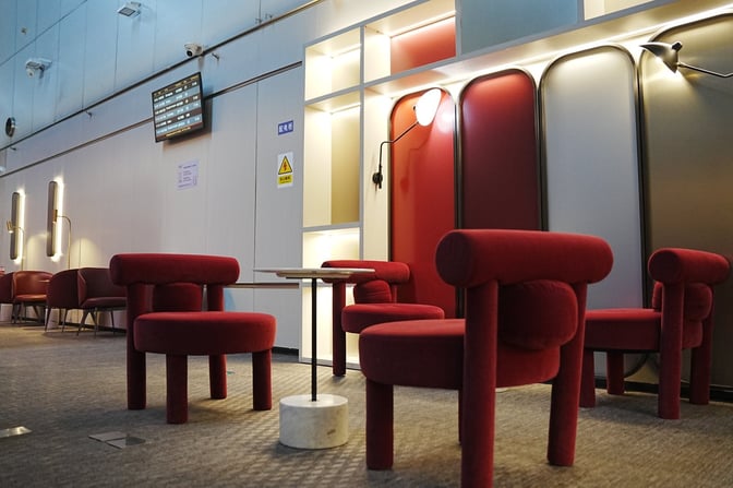 The seating area in Beijing Capital V6 Lounge features individual chairs and small tables, with a flight information screen overhead.