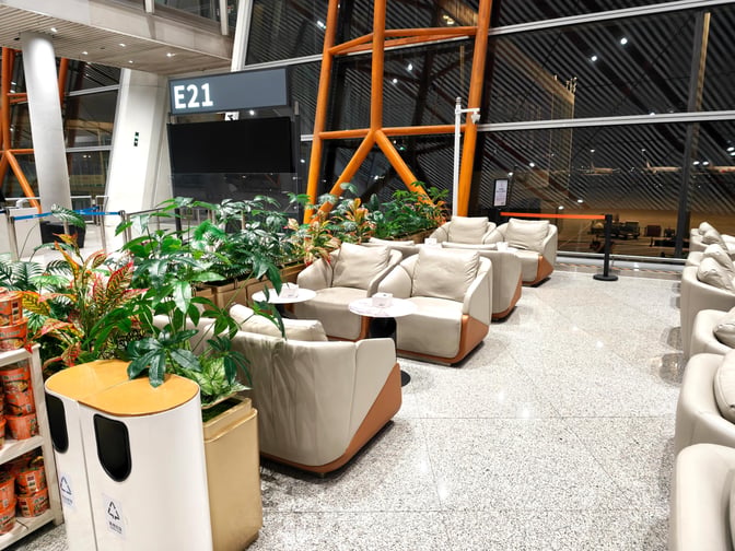 Seating area at CIP International Lounge, Beijing Capital Airport, features comfortable chairs and small tables near Gate E21 with airport views.