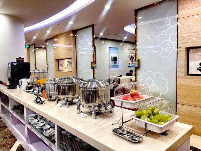 The Trvok A1 Lounge at Beijing Capital International Airport features a self-serve food station with hot dishes, fruits, and beverages.
