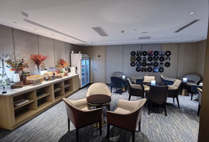 The CHUM Courtesy Lounge at Beijing Daxing International Airport features a seating area with tables and a self-serve snack station.