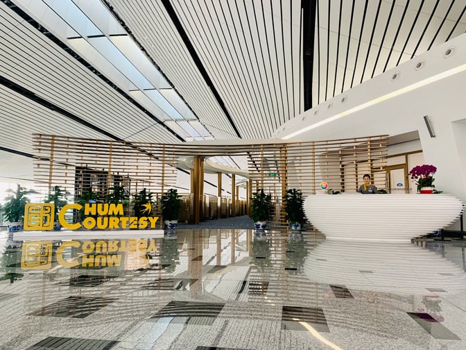 The CHUM International Lounge entrance at Beijing Daxing Airport features a reception desk and decorative plants, welcoming travelers.