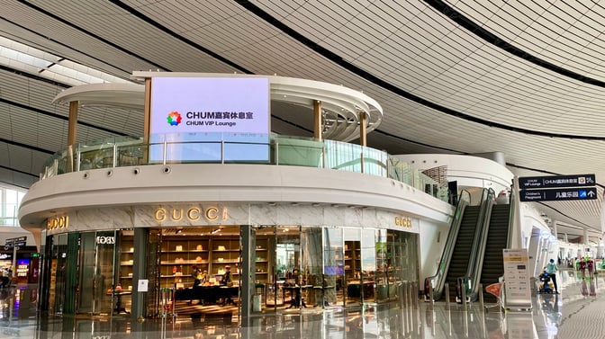 The CHUM VIP Lounge at Beijing Daxing International Airport is located above a retail area, accessible via escalator.
