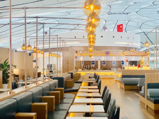 The China Eastern Airlines V5 Lounge at Beijing Daxing International Airport features spacious seating with tables and a visible service counter.