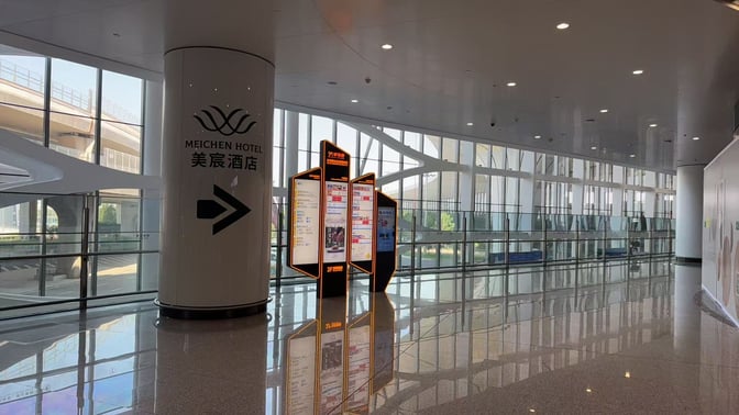 The Meichen VIP Lounge entrance at Beijing Daxing International Airport is marked by signage and digital information displays near a large window.