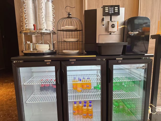 The Meichen VIP Lounge at Beijing Daxing International Airport features a beverage station with a coffee machine and refrigerated soft drinks.